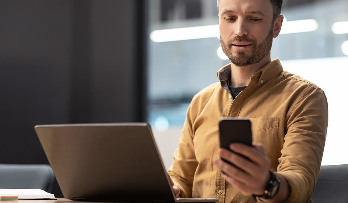 Image of man using his phone and laptop at work.
